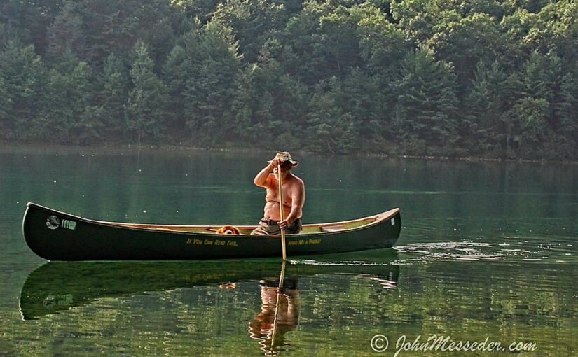 Canoe and paddler floats on a clear lake