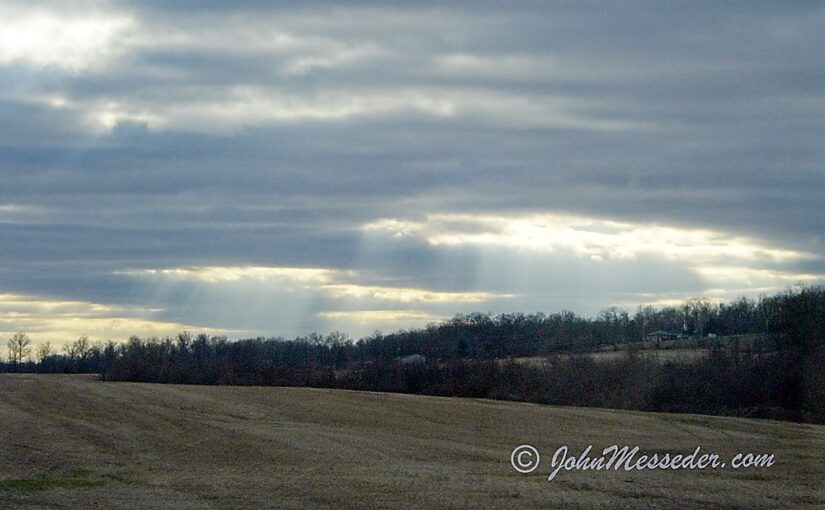 Sun beams shining through a near overcast onto a future cornfield